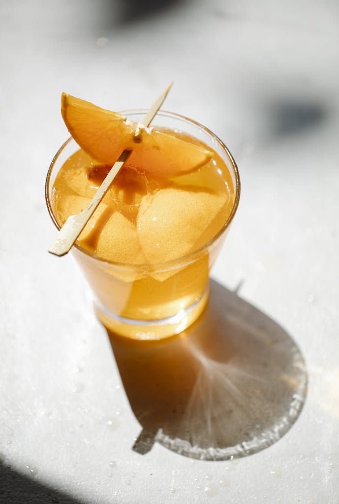Chilled orange cocktail with slices and stick garnish in a sunbeam on a table.