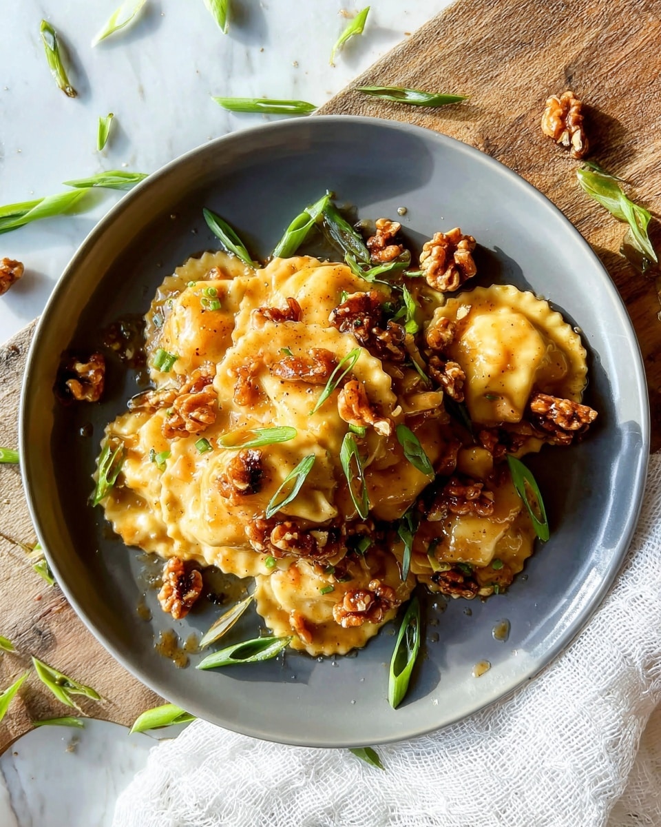 A gray plate holds a layered dish of golden-brown ravioli with a slightly crispy texture on the edges, each piece covered in a glossy, light brown sauce. Scattered on top and around the ravioli are uneven pieces of toasted walnuts, deep brown in color and with a textured surface. Bright green sliced scallions are placed stylishly on top and around the dish, adding a fresh contrast. The plate sits on a white marbled surface with scattered scallion pieces and a white textured cloth partially visible on the right side. Photo taken with an iphone --ar 4:5 --v 7