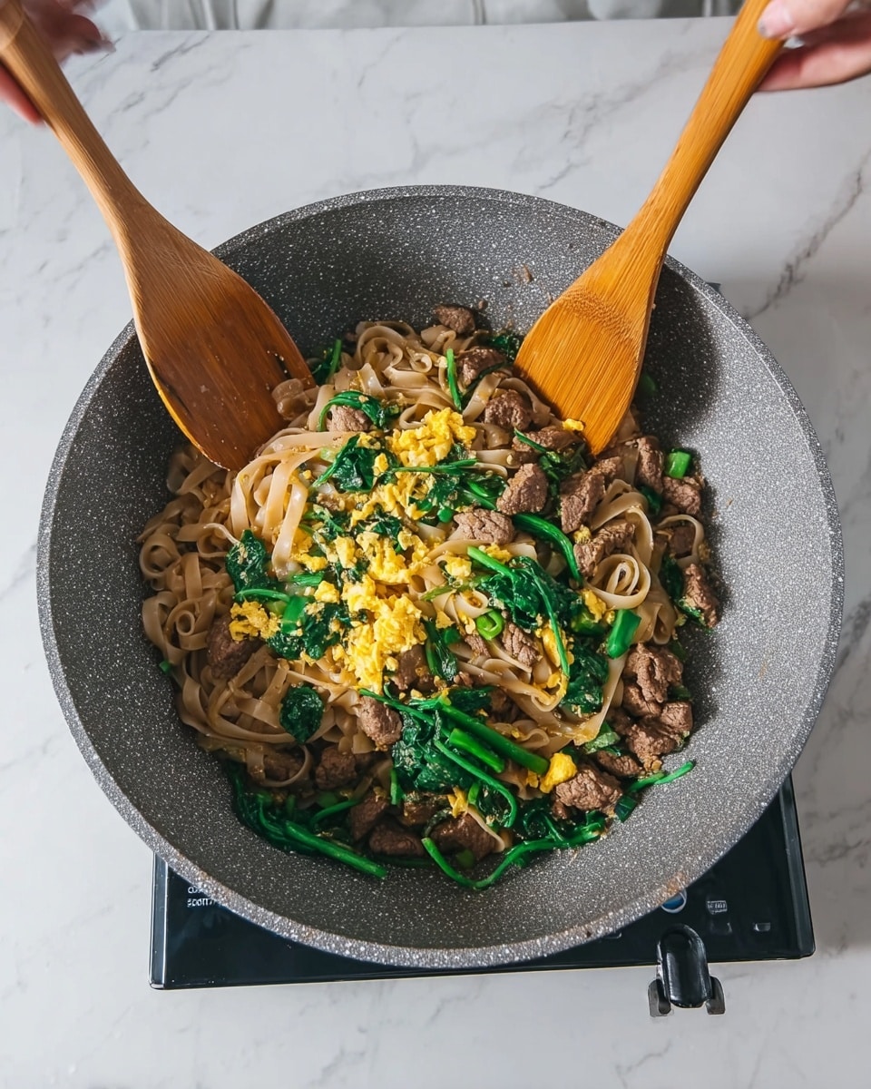 A white bowl filled with wide, flat noodles that are light brown and glossy, mixed with dark brown pieces of cooked beef and vibrant green leafy vegetables. Small chunks of scrambled egg in a light golden color are scattered evenly throughout the dish. The bowl sits on a white cloth on a surface with a white marbled texture. On the top right, there are white chopsticks with light wooden tips resting on the surface, along with stacked white plates. A clear glass cup is placed to the top left side of the bowl. The whole scene is bright and clean. photo taken with an iphone --ar 4:5 --v 7