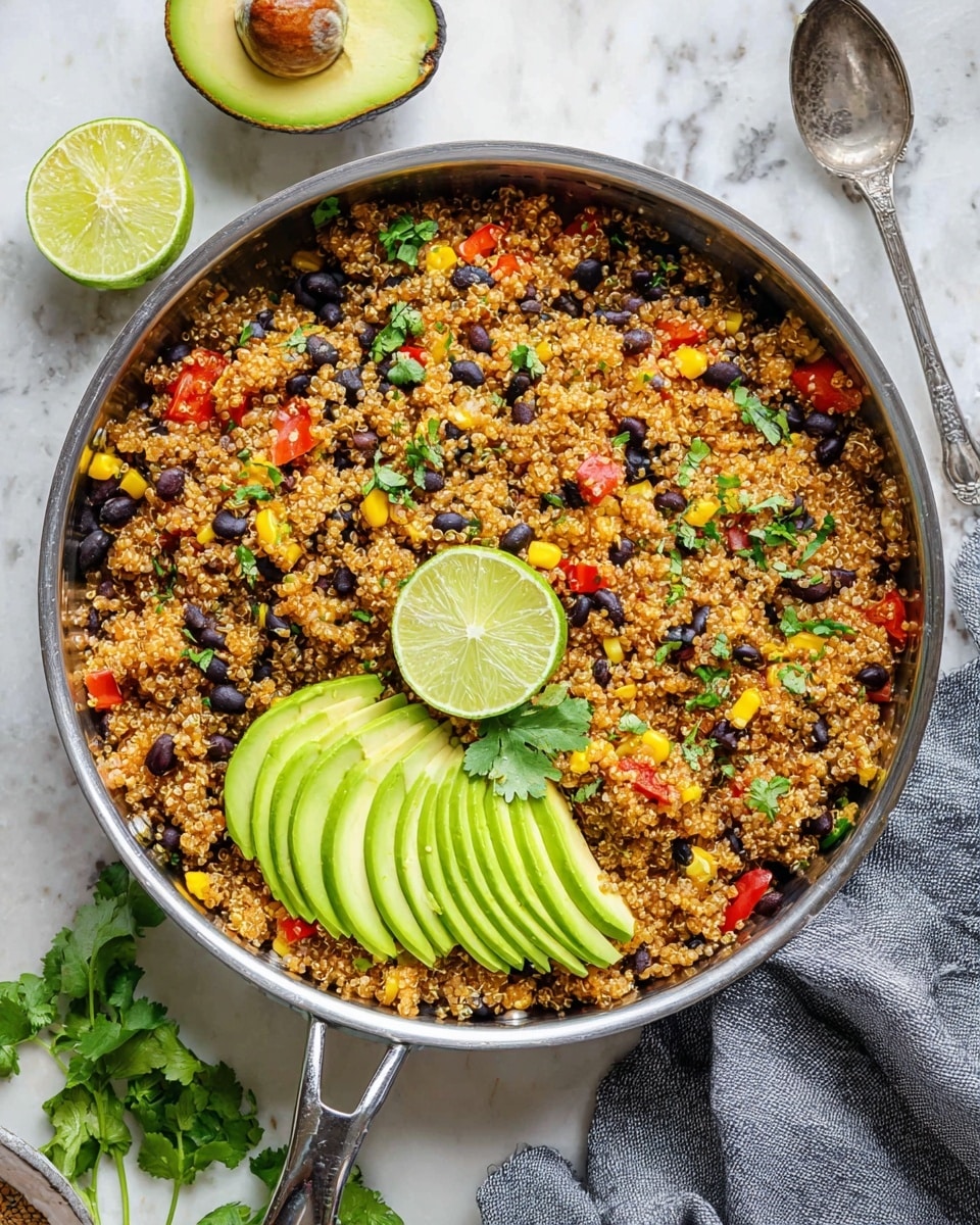 A silver pan filled with a colorful quinoa dish showing small grains of light brown quinoa mixed with black beans, yellow corn, and red bell pepper pieces, all topped with green chopped cilantro. On one side of the pan, three slices of fresh avocado are neatly fanned out bright green and smooth in texture, and in the center, two lime wedges with a small sprig of cilantro rest on the quinoa. The pan is placed on a white marbled surface with a halved avocado and lime nearby, and a gray cloth with a silver spoon is partially visible to the right. Photo taken with an iphone --ar 4:5 --v 7