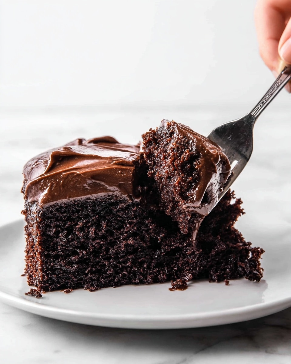 A close-up view of a single thick slice of chocolate cake on a white plate, showing two layers: a bottom layer of dark, moist, crumbly chocolate cake, and a top layer of smooth, glossy chocolate frosting that slightly drips over the cake’s edge, all set on a white marbled surface, photo taken with an iphone --ar 4:5 --v 7