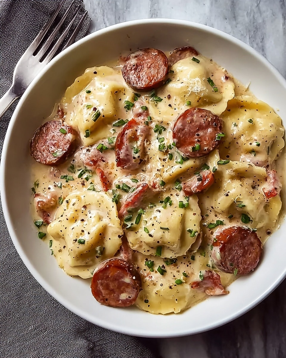 In a white bowl, there is a creamy pasta dish made of round ravioli pieces that are pale yellow and smooth with some light browning on the edges. Scattered throughout the ravioli are thick slices of browned sausage with a reddish-brown color and a slightly crispy outside. The creamy sauce coats the ravioli and sausage, having a pale beige tone with a smooth and slightly glossy texture. Chopped green herbs are sprinkled on top, adding small bright green spots for contrast. There are tiny black pepper flakes spread across the dish, adding small dark specks. The bowl sits on a white marbled surface with a silver fork and a gray cloth napkin beside it. Photo taken with an iphone --ar 4:5 --v 7