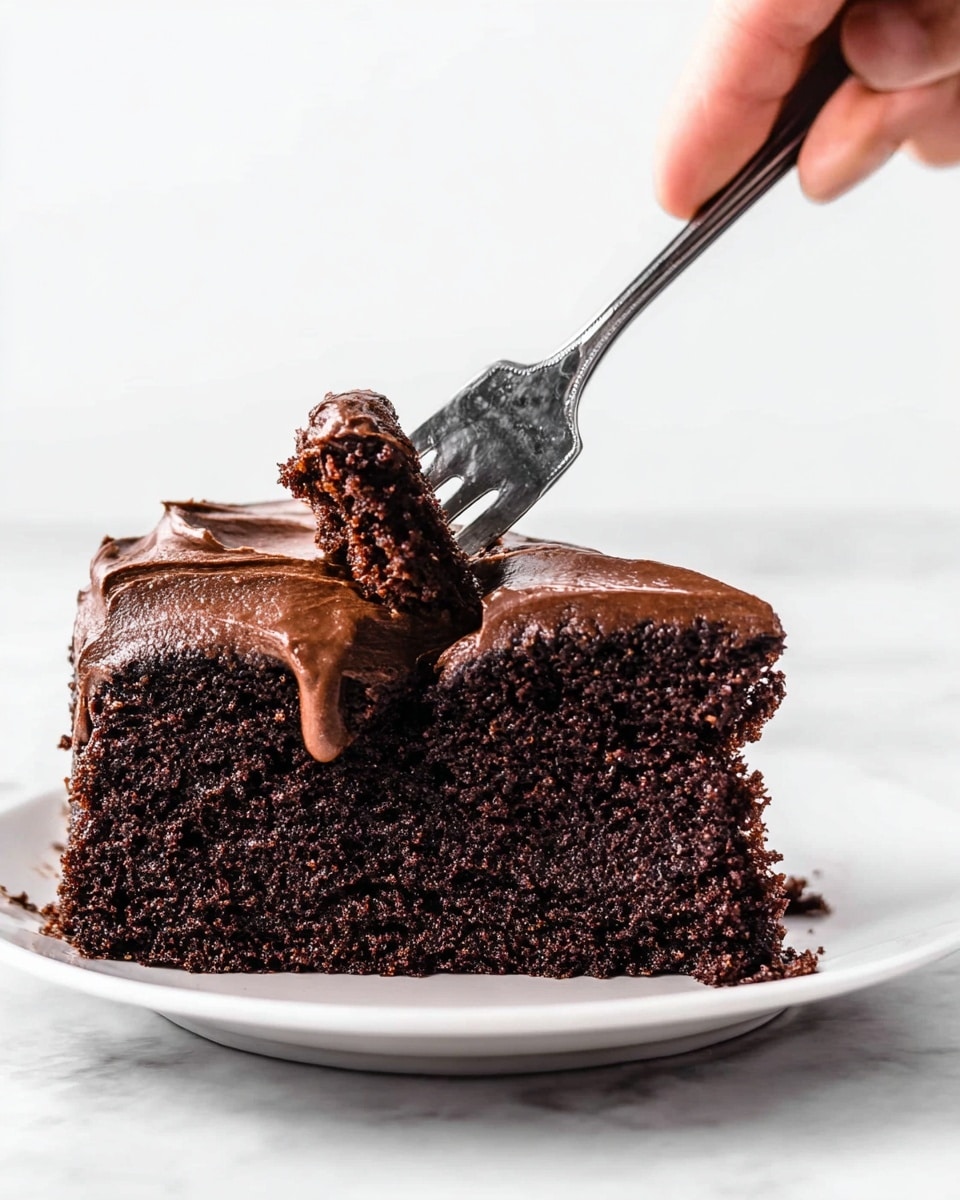A thick slice of dark brown chocolate cake with a moist, crumbly texture forms the base layer. On top, a thick layer of smooth, glossy chocolate frosting with soft peaks and drips slightly over the edges. A woman’s hand is holding a fork, cutting into the cake slice, lifting a bite with visible crumb detail. The slice is placed on a white plate, set against a white marbled surface. photo taken with an iphone --ar 4:5 --v 7