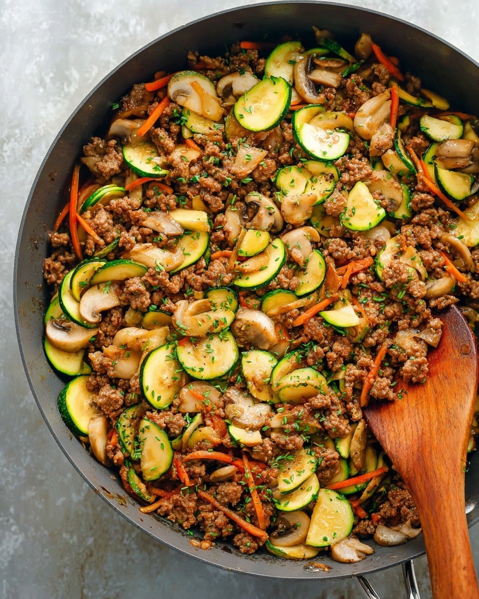 A close-up of a large grey pan filled with cooked ground meat, mixed with sliced green zucchini, light brown sliced mushrooms, and thin strips of orange carrot. The ingredients are evenly spread and look moist and well-cooked, with small green herb pieces sprinkled on top. A wooden spoon is placed inside the pan on the right side, touching the food. The pan is sitting on a white marbled textured surface. photo taken with an iphone --ar 4:5 --v 7