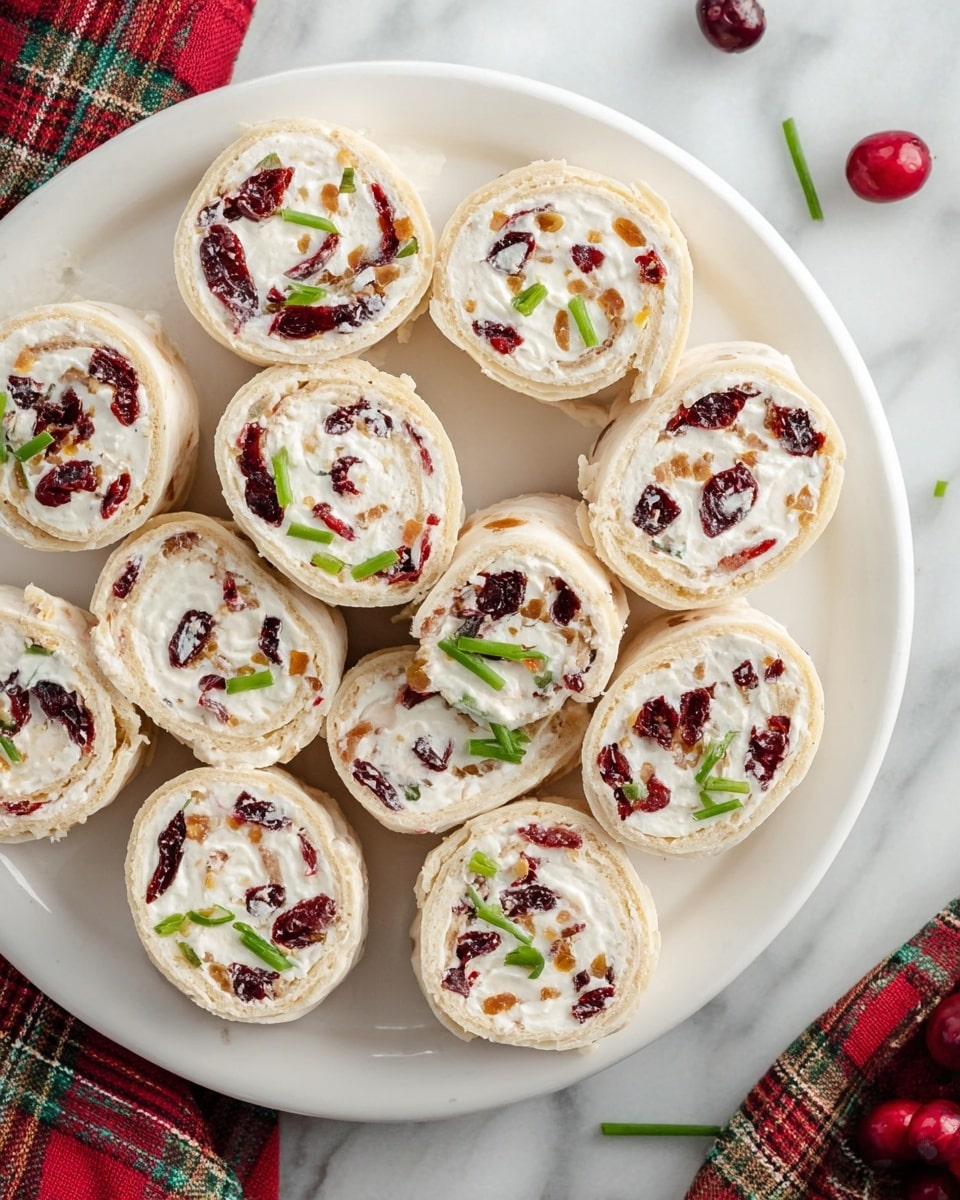 A white round plate holds about twelve pinwheel roll-ups arranged close together, each roll-up showing two main layers: a light beige outer tortilla or bread layer, and a white creamy filling mixed with small bits of dark red dried cranberries and green chopped scallions unevenly spread inside. The rolls are sliced to show the spiral pattern of the layers, with the red and green bits adding color contrast inside the white filling. The plate sits on a white marbled surface with a red and green plaid cloth nearby and a few scattered pieces of cranberries and scallions around. Photo taken with an iphone --ar 4:5 --v 7