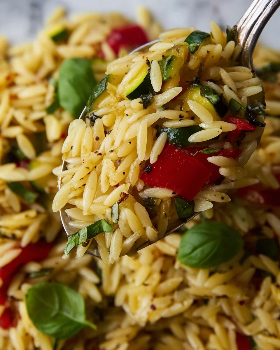 A white bowl filled with a single layer of orzo pasta mixed with small pieces of red bell pepper, green zucchini, and fresh green basil leaves scattered on top, all coated lightly with herbs and spices giving a speckled look. A silver fork with black handles is resting in the bowl on the right side, partially covered by the orzo. The bowl sits on a white marbled surface, and in the background on the right is a small white square dish with green sauce. Photo taken with an iphone --ar 4:5 --v 7