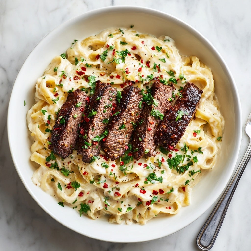 A white bowl filled with creamy fettuccine pasta covered in a thick white sauce, garnished with finely chopped green herbs. On top of the pasta, there are five slices of grilled steak with a rich brown color and a slightly charred texture. Red chili flakes and more green herbs are sprinkled over the steak and pasta, adding spots of red and green throughout. The bowl sits on a white marbled surface, with a silver fork nearby. Photo taken with an iphone --ar 4:5 --v 7
