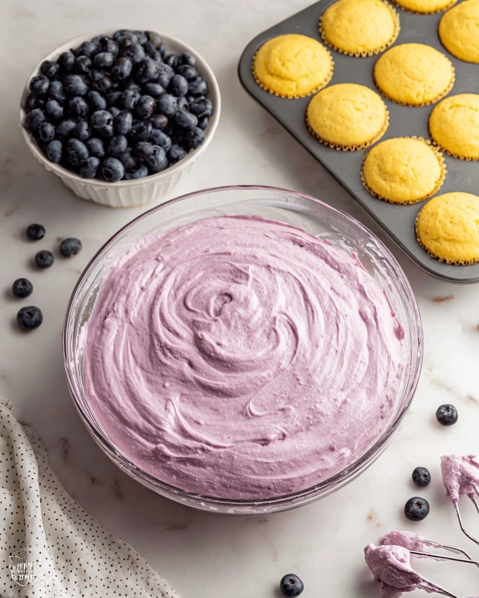 The image shows a close-up of four vanilla cupcakes on a white plate with a white marbled texture background. Each cupcake has two layers: the bottom layer is a soft and fluffy pale yellow cake with a slightly crumbly texture, and the top layer is a thick swirl of light purple frosting with visible darker purple flecks, giving it a creamy and textured look. The cupcake in the front is unwrapped and partially eaten, showing the inside crumb clearly. The frosting is piped with a decorative swirl pattern, and the overall presentation looks fresh and inviting. Photo taken with an iphone --ar 4:5 --v 7