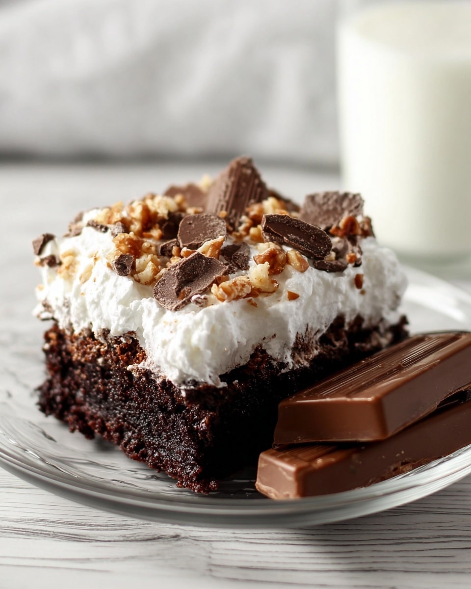 A close-up of a moist, dark brown chocolate cake with one thick layer topped with a generous spread of fluffy white whipped cream that looks soft and creamy. On top of the whipped cream, there are small chopped pieces of light brown and darker chocolate candy bars scattered unevenly, adding a crunchy texture. The cake is placed on a white marbled surface. Photo taken with an iphone --ar 4:5 --v 7