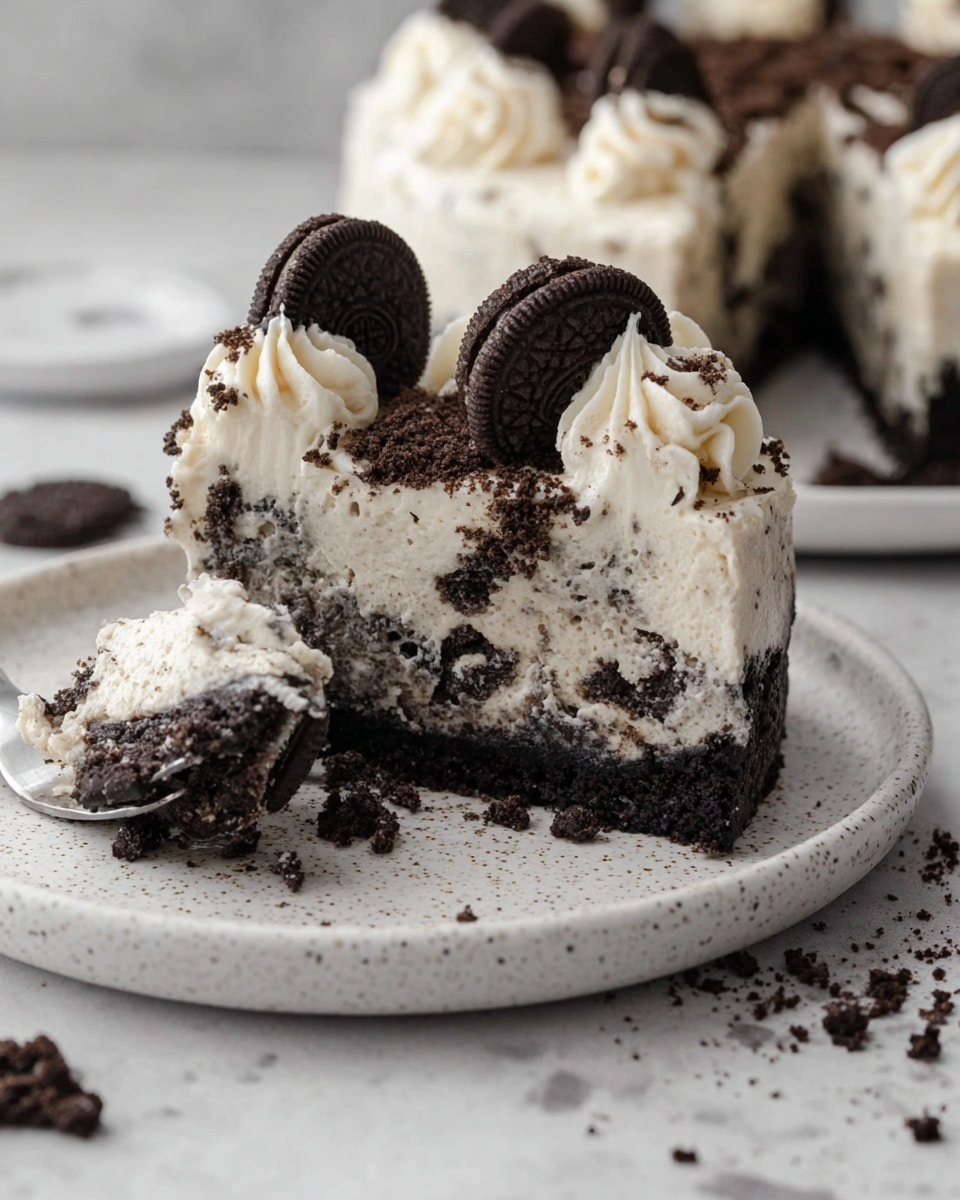 The image shows a slice of cookies and cream cheesecake on a white speckled plate. The bottom layer is a thick, crumbly dark chocolate cookie crust. Above it is a thick, creamy white cheesecake layer with crushed dark cookie pieces mixed inside, giving it a marbled look. On top of the cheesecake slice is a smooth creamy white layer with piped swirls of whipped cream. Each swirl is topped with a small chocolate sandwich cookie, and there are small cookie crumbs sprinkled over the top and around the plate. A bite-sized piece of the cheesecake is on a fork next to the slice. The setting is on a white marbled texture surface. photo taken with an iphone --ar 4:5 --v 7