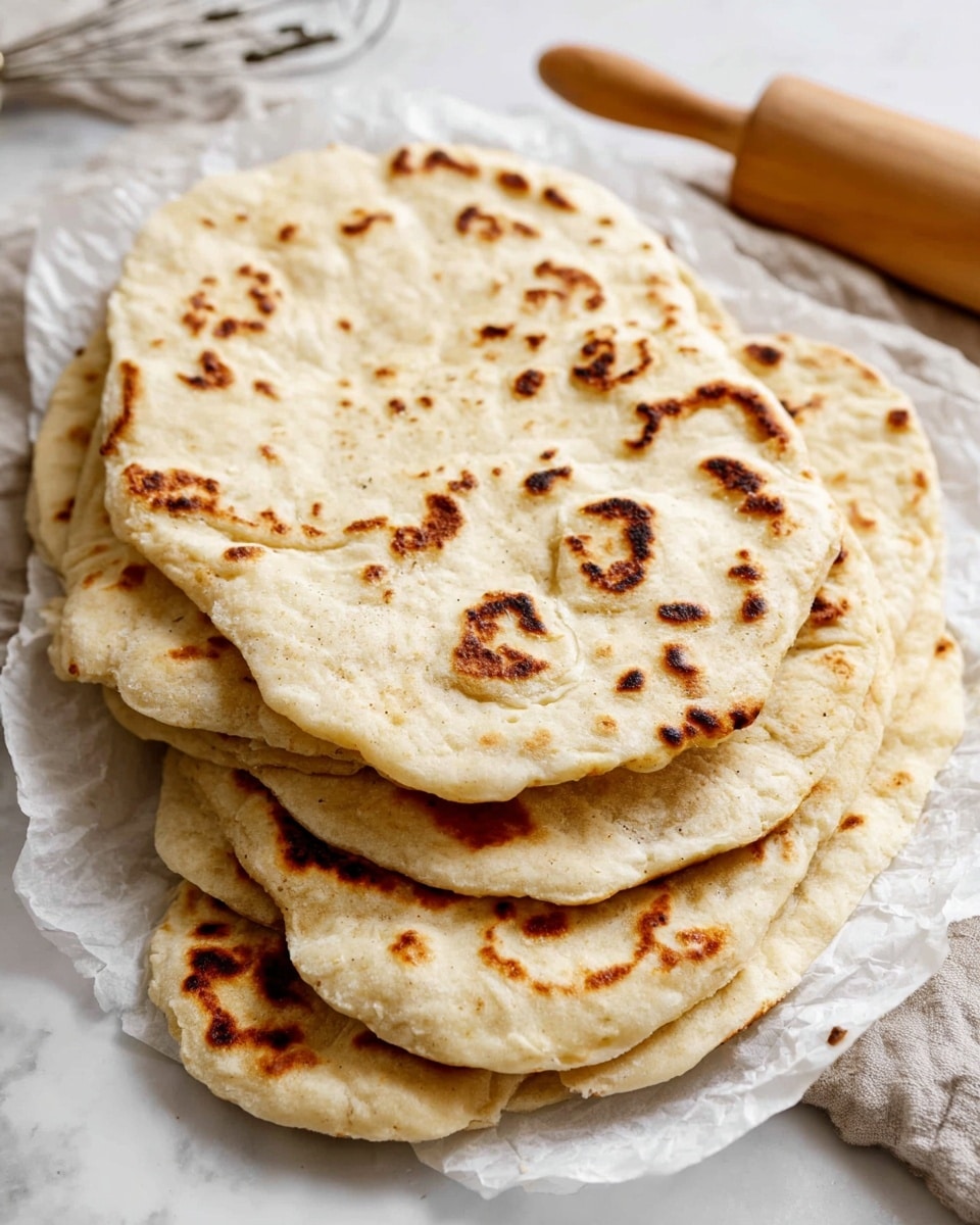 A close-up view of a stack of flatbreads shows six pieces layered unevenly on a white marbled surface, each flatbread having a light golden-brown color with scattered darker char marks and a soft, slightly puffy texture. The edges are uneven and slightly thicker, with some folds visible, giving them a rustic and handmade look. The flatbreads are arranged so that parts of each one overlap the next, creating a layered effect that highlights their thin, flexible nature. photo taken with an iphone --ar 4:5 --v 7