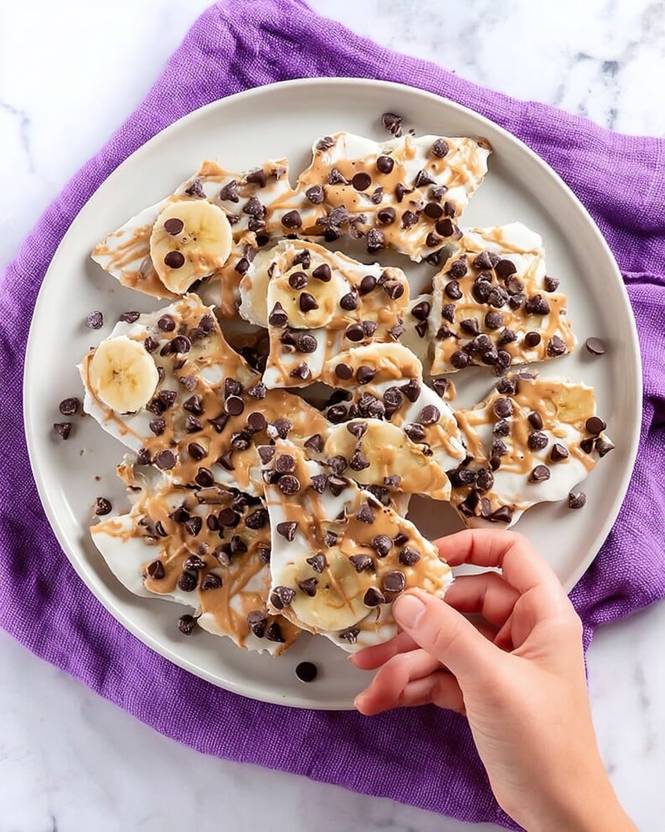 A white plate filled with pieces of frozen yogurt bark, each piece showing three distinct layers: a thick bottom layer of creamy white frozen yogurt, a middle drizzle layer of light brown peanut butter swirled on top, and a scattering of small dark chocolate chips across the surface. On top of each piece, there are round slices of yellow banana evenly placed, adding a fresh look. The plate sits on a purple cloth with white dots, all over a white marbled texture background. photo taken with an iphone --ar 4:5 --v 7