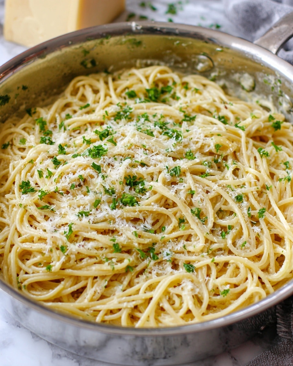 A close-up of creamy spaghetti on a white plate showing one layer of light golden pasta coated evenly in a smooth, creamy white sauce. The spaghetti is sprinkled with small bits of white grated cheese and bright green chopped parsley scattered on top, adding color and texture. The pasta strands are slightly glossy with sauce and look soft with some small pepper specks visible. A silver fork rests on the edge of the plate, all set on a white marbled surface. photo taken with an iphone --ar 4:5 --v 7