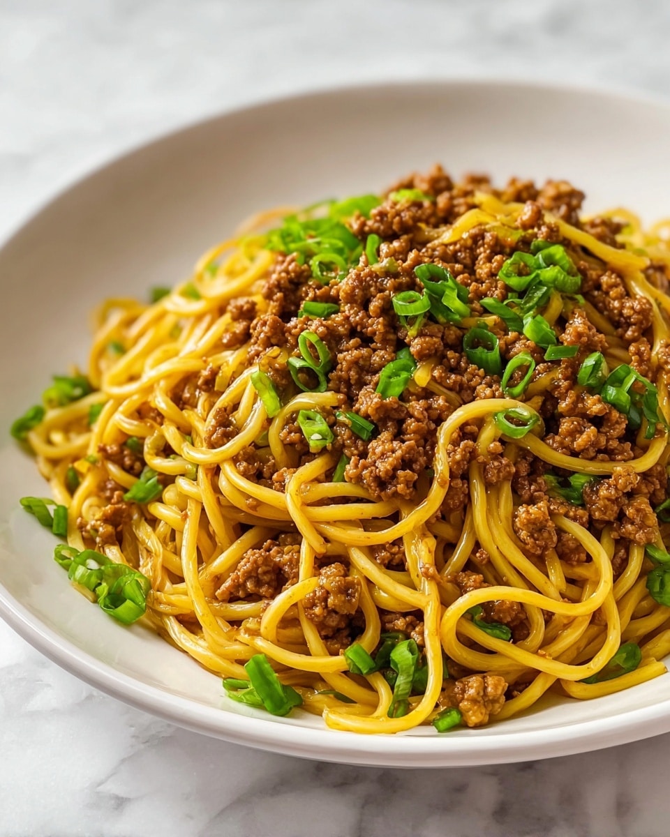 A white plate holds a serving of noodles mixed with ground meat, each noodle shiny and yellowish-brown, twisted together in loose, thick strands. The brown cooked ground meat is spread evenly across the noodles, giving a textured, crumbly look. Bright green chopped scallions are sprinkled on top and around the edges, adding vibrant color contrast to the dish. The plate sits on a white marbled surface, enhancing the warm tones of the food. photo taken with an iphone --ar 4:5 --v 7