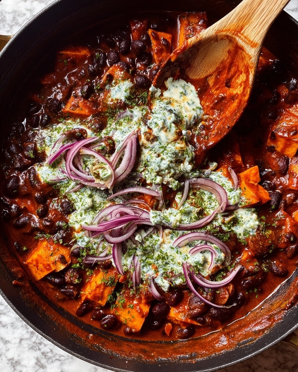 A thick stew with two main layers in a large white pot with an orange rim; the bottom layer is dark red sauce mixed with black beans and bright orange chunks of cooked sweet potato, showing a rich and hearty texture; the top layer has caramelized red onions with shiny, soft, and slightly translucent edges, scattered over the stew, and dollops of white cream sauce streaked with green herbs adding contrast; the inside walls of the pot are stained with thick red sauce, and a wooden spoon is partially dipped into the stew, the photo taken on a white marbled surface; photo taken with an iphone --ar 4:5 --v 7